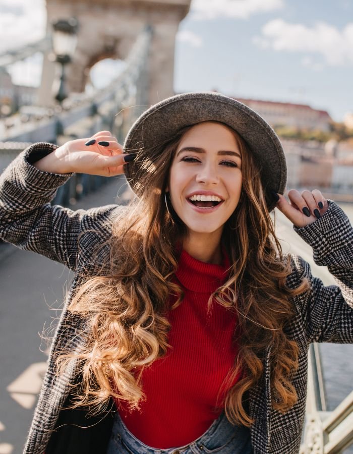 Mulher sorridente de chapéu numa ponte histórica na Europa